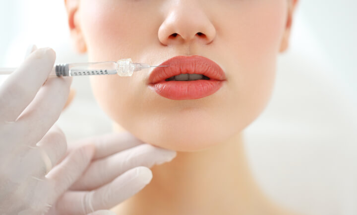 woman showing her plump lips and receiving an injection of dermal fillers