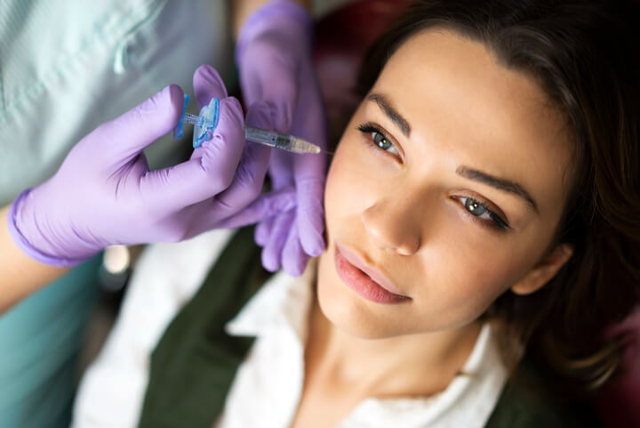 woman receiving dermal fillers injection under eyes by professional medical doctor