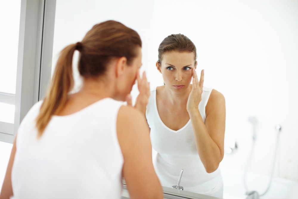woman in front of the mirror looking at her under eye area