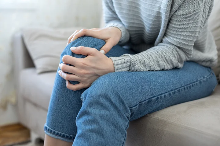Woman seating holding knees suffering from knee joint pain